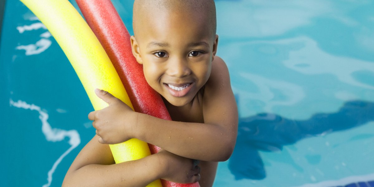 Child holding pool noodle in pool